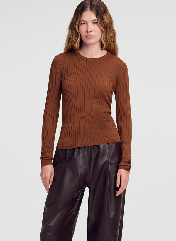 A woman modeling a brown ribbed long-sleeve knit top with dark wide-leg pants against a light gray studio background.