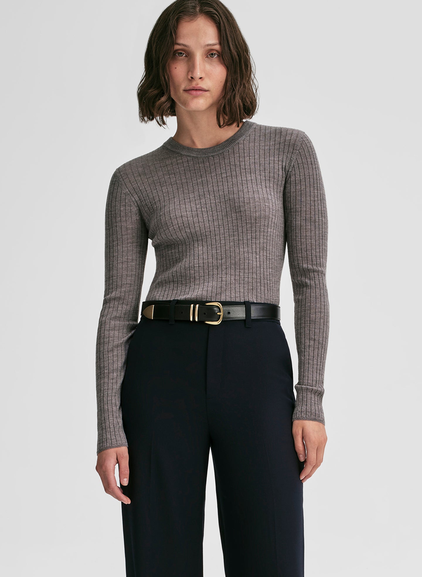 Woman wearing a gray ribbed sweater and black pants on a light gray background