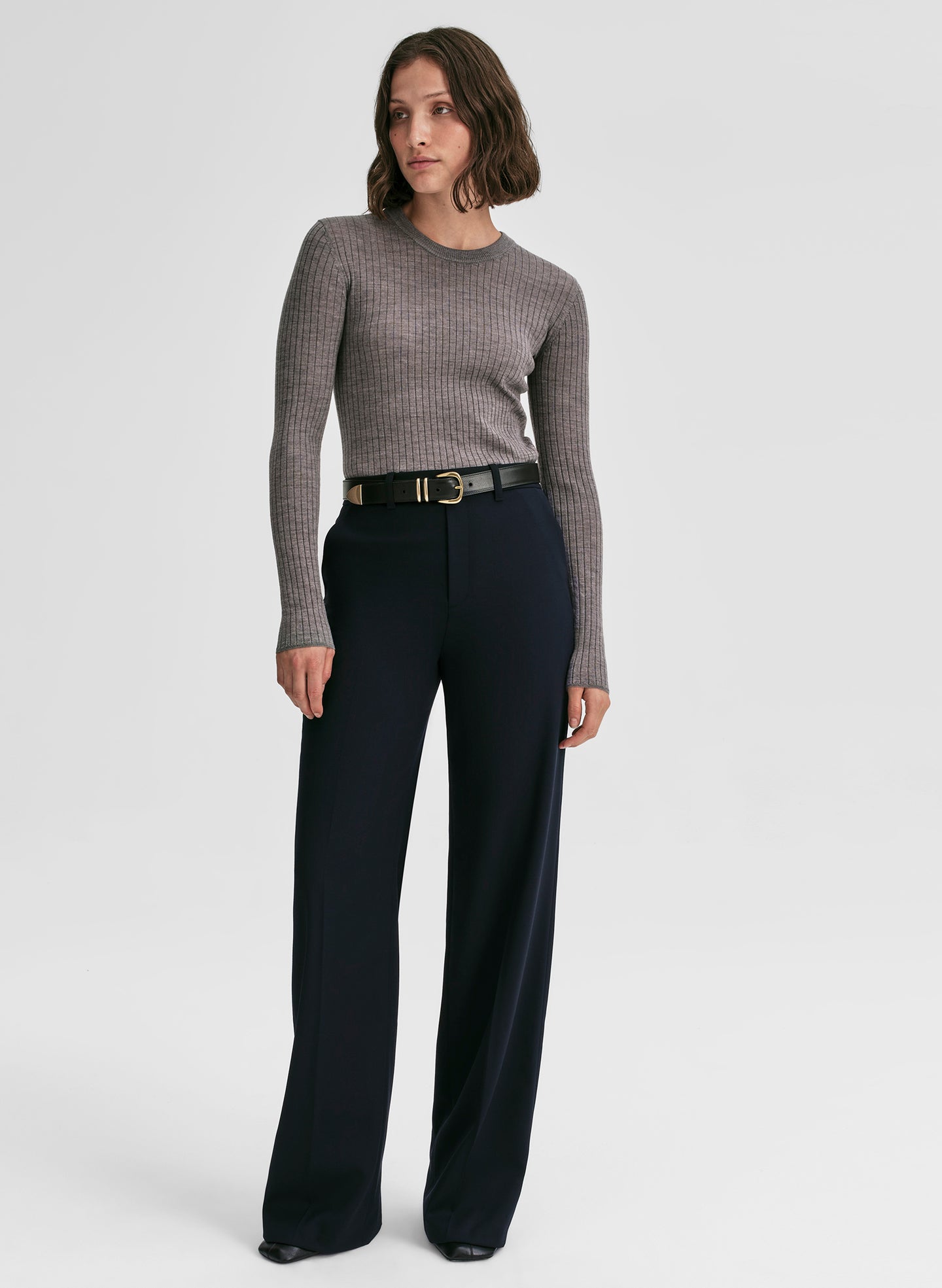 Woman wearing a gray sweater and black pants on a white background