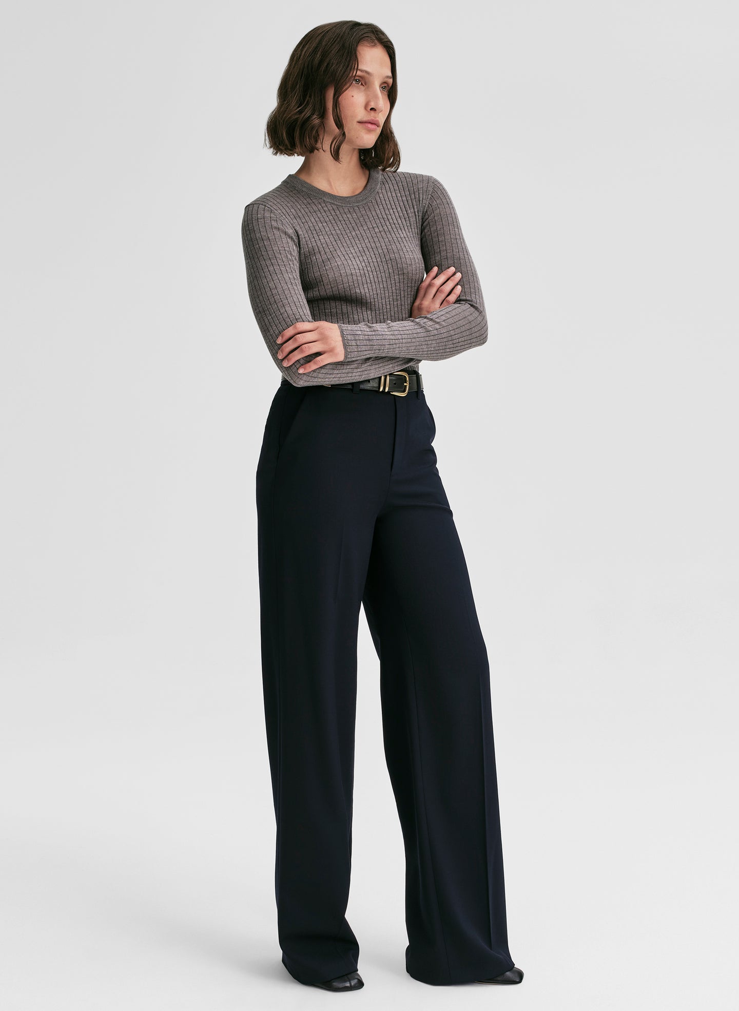 Woman wearing a gray sweater and black pants on a white background
