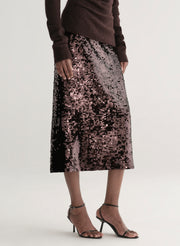 Woman wearing a brown off-shoulder top and sequin midi skirt on a white background