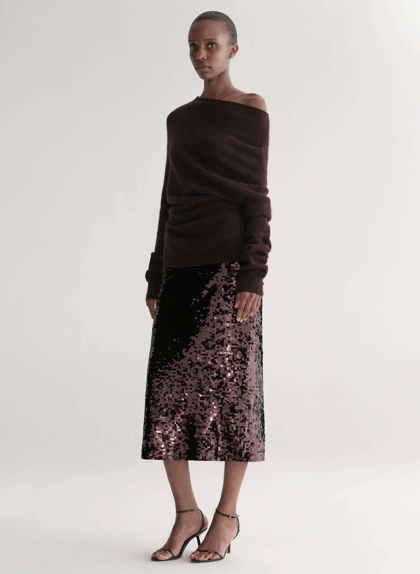 Woman wearing a brown off-shoulder top and sequin midi skirt on a white background