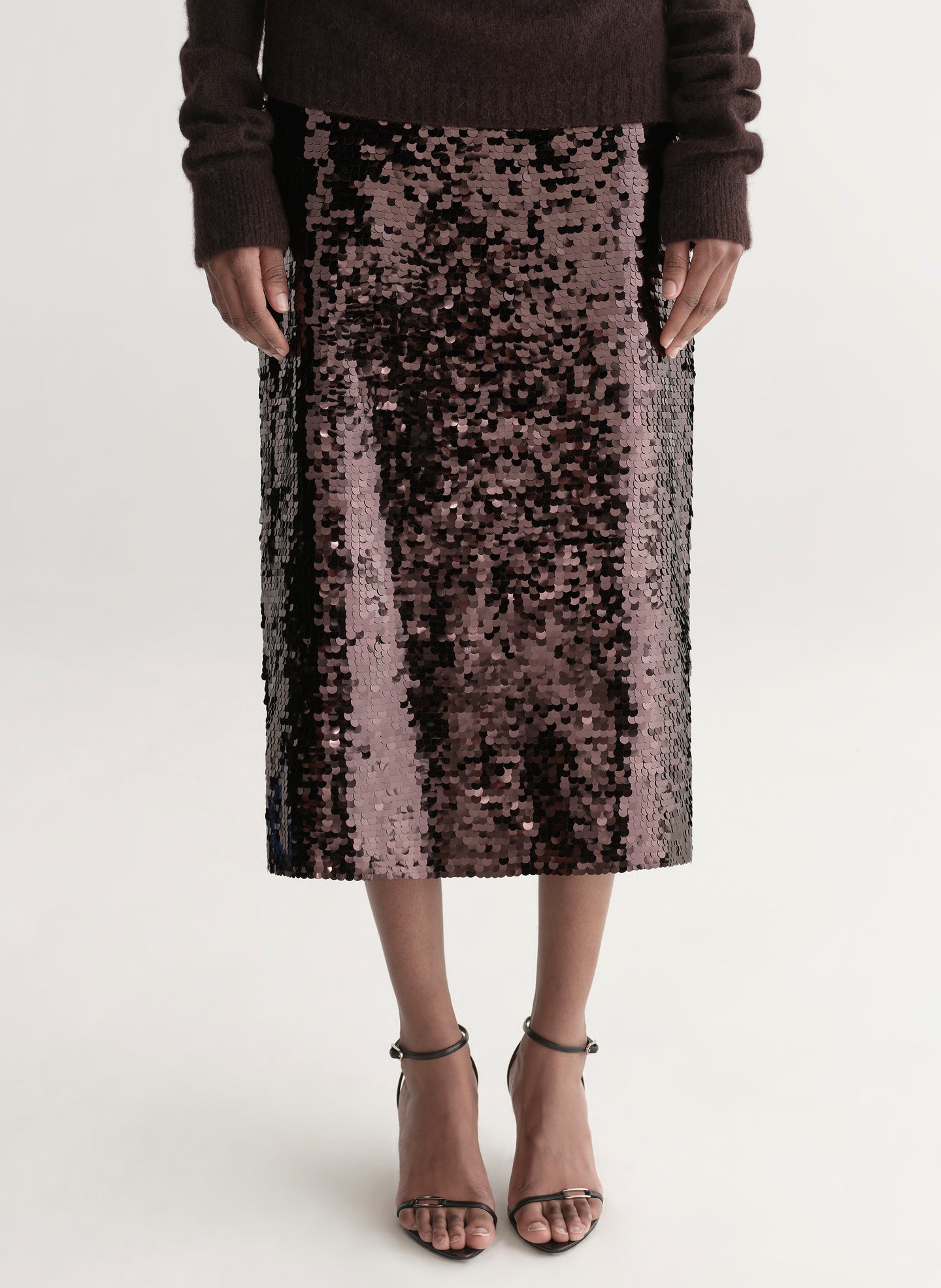 Woman wearing a brown off-shoulder top and sequin midi skirt on a white background