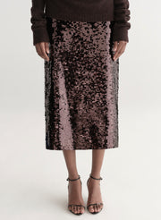 Woman wearing a brown off-shoulder top and sequin midi skirt on a white background