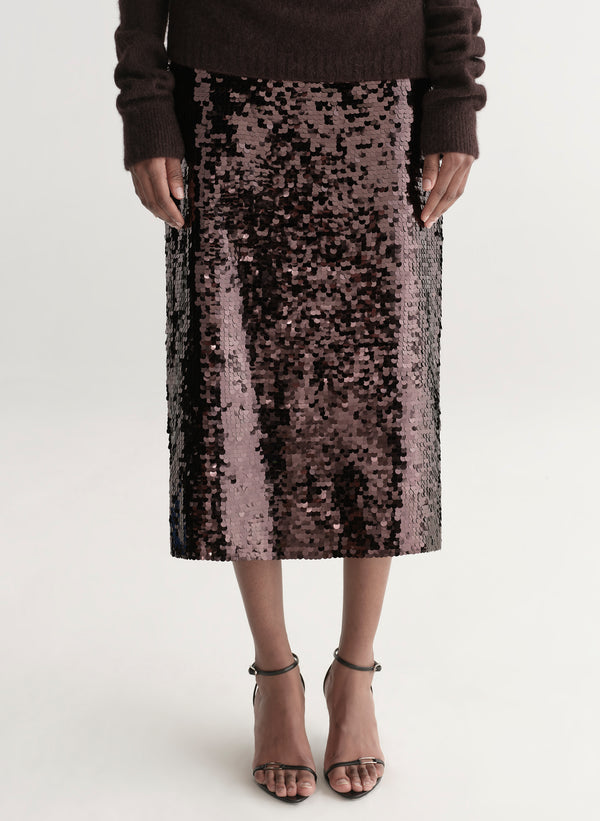 Woman wearing a brown off-shoulder top and sequin midi skirt on a white background