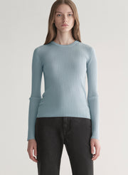 Woman wearing a light blue ribbed top and black denim pants on a plain background