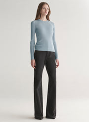 Woman wearing a light blue ribbed top and black denim pants on a plain background