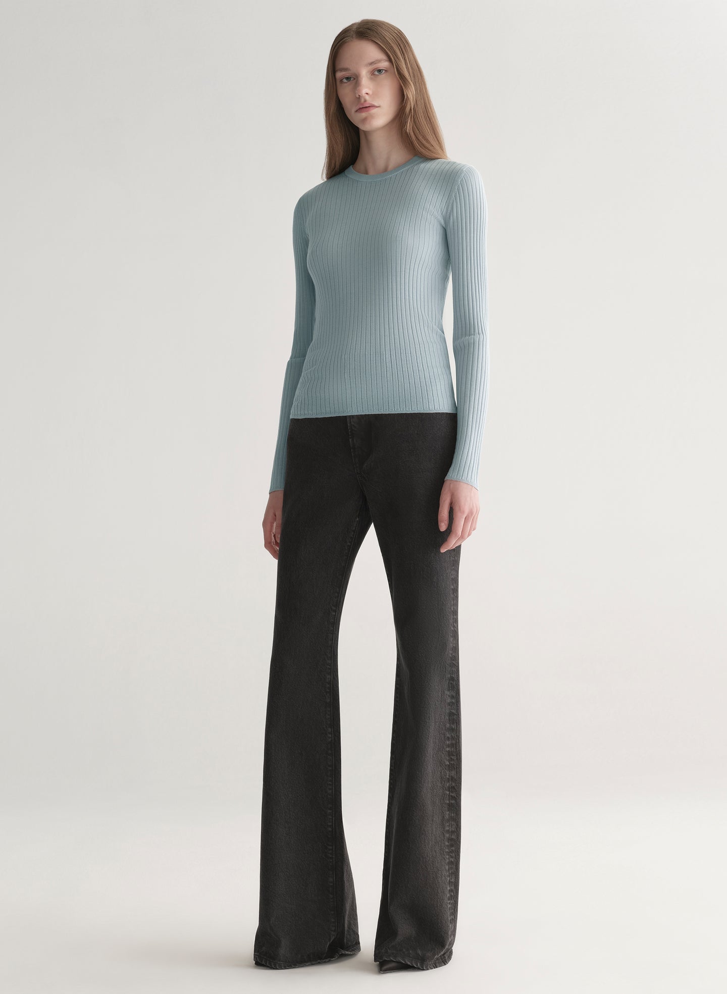 Woman wearing a light blue ribbed top and black denim pants on a plain background