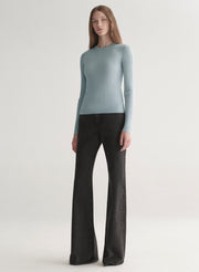 Woman wearing a light blue ribbed top and black denim pants on a plain background