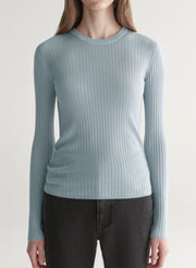 Woman wearing a light blue ribbed top and black denim pants on a plain background