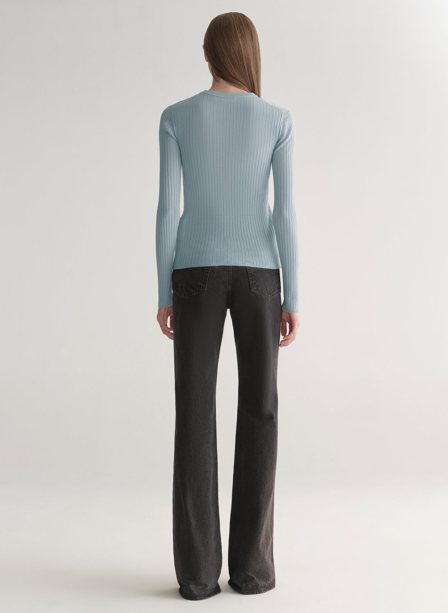 Woman wearing a light blue ribbed top and black denim pants on a plain background