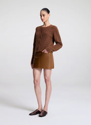 Woman wearing a brown knitted cardigan and leather skirt on a white background
