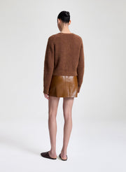 Woman wearing a brown knitted cardigan and leather skirt on a white background