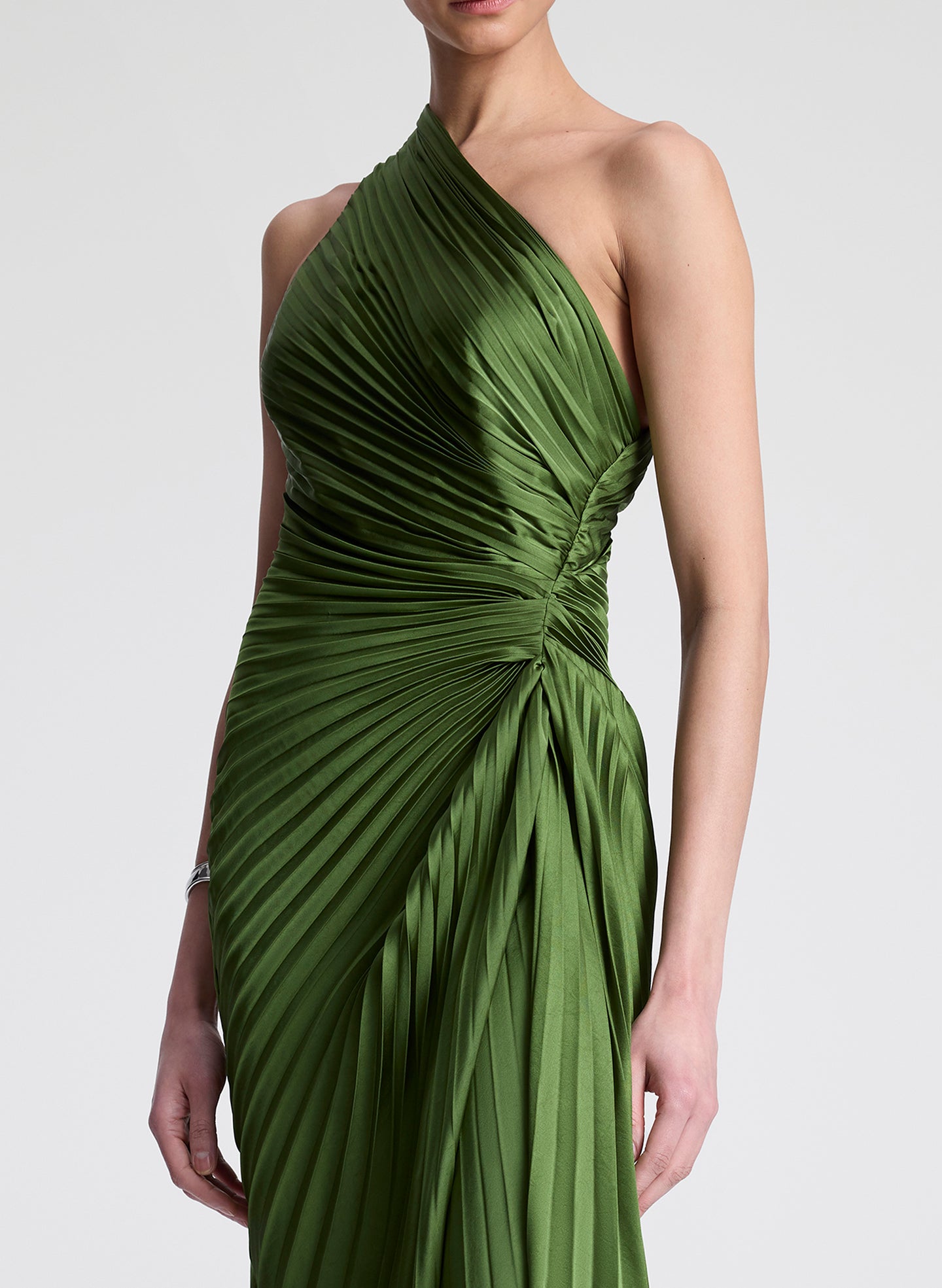 Woman wearing a green one-shoulder pleated dress on a white background