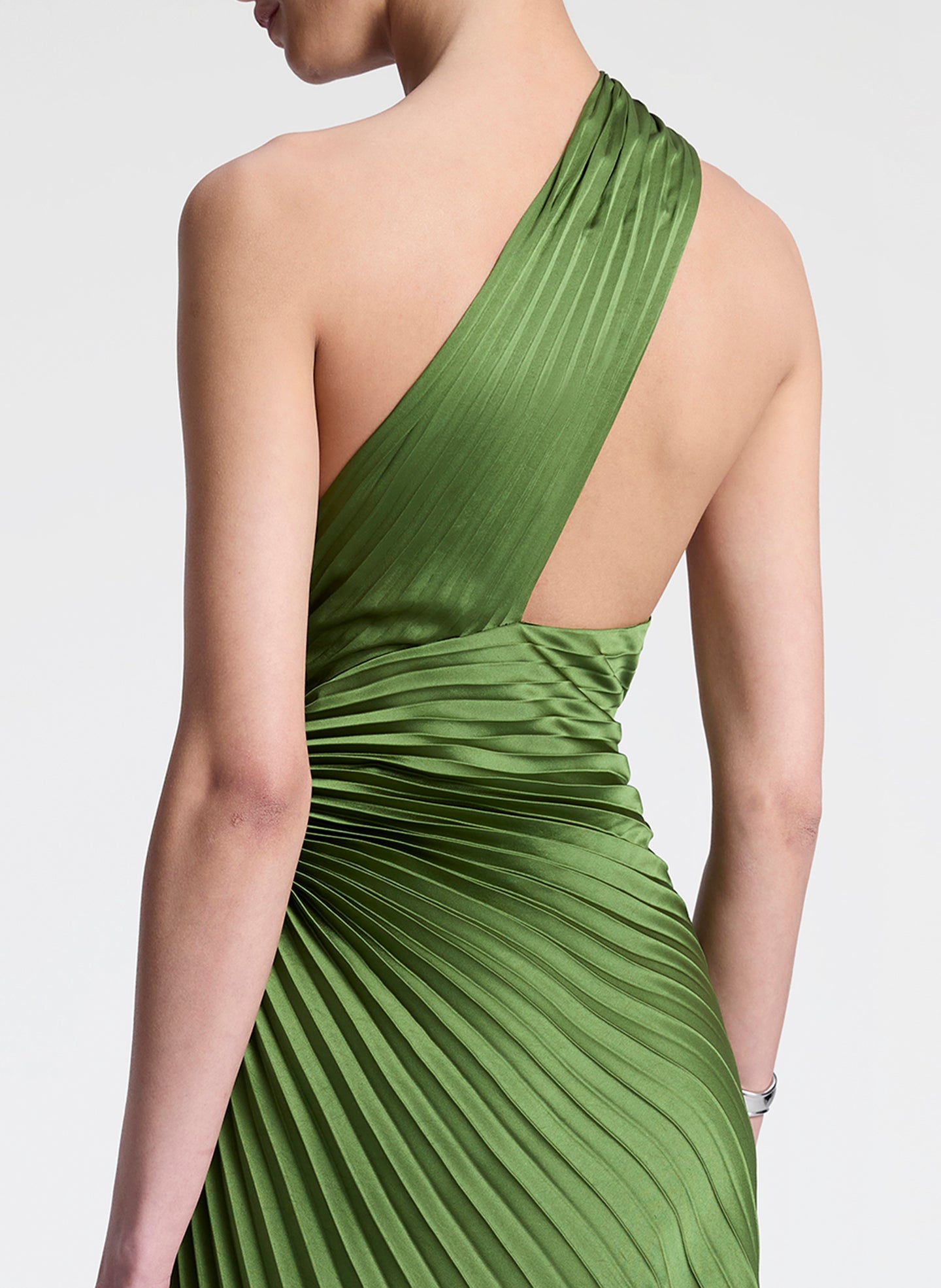 Woman wearing a green one-shoulder pleated dress on a white background