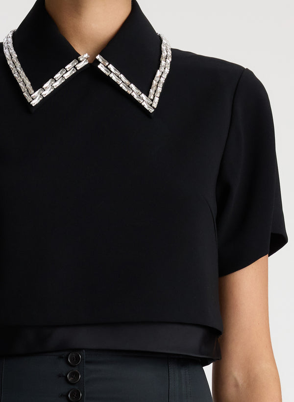 detail view of woman wearing black short sleeve collared top with crystal detailing and black pants