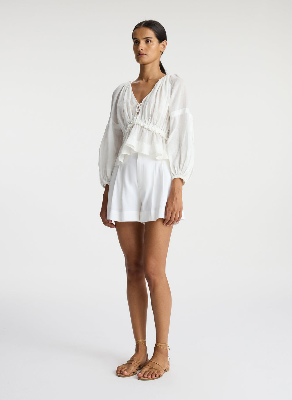 side view of woman wearing white v neck blouse with peplum and white shorts