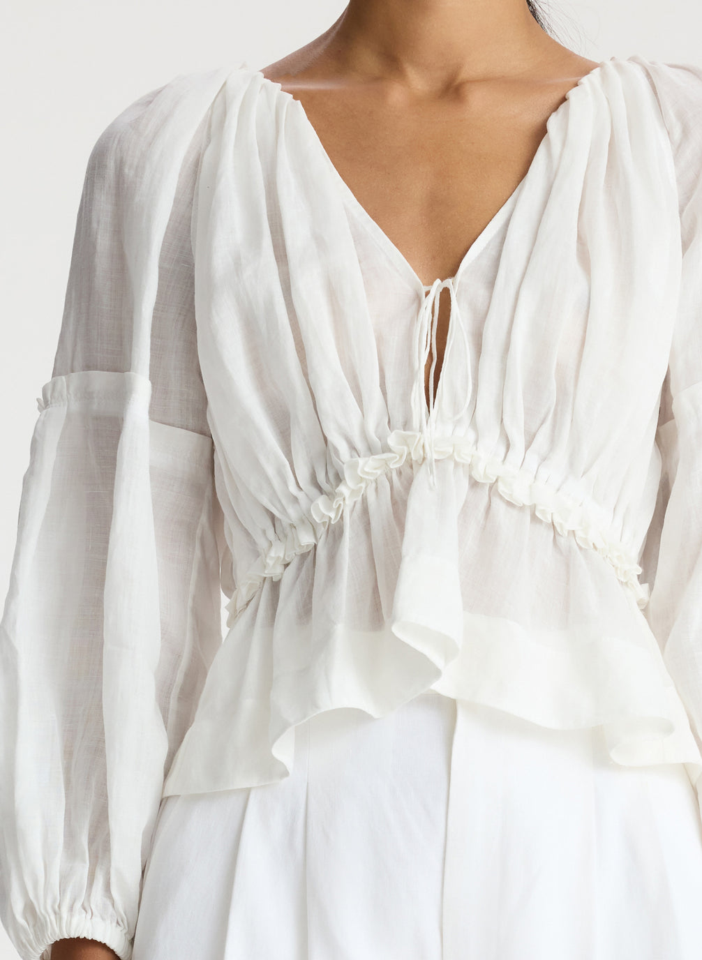 detail view of woman wearing white v neck blouse with peplum and white shorts