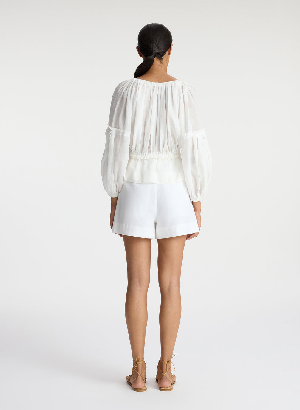 back view of woman wearing white v neck blouse with peplum and white shorts