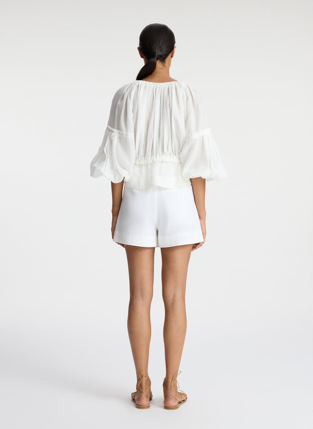 back view of woman wearing white blouse and white shorts