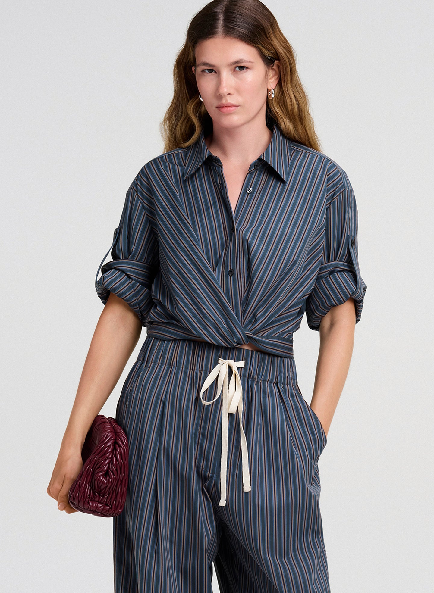 Woman wearing a striped top and pants holding a red purse against a white background