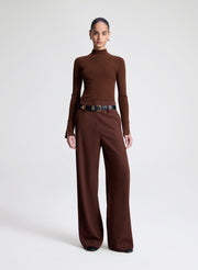 Woman wearing a brown turtleneck and wide-leg pants on a white background
