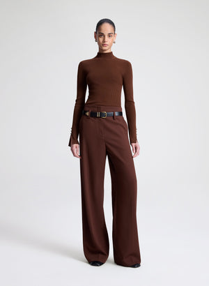 Woman wearing a brown turtleneck and wide-leg pants on a white background