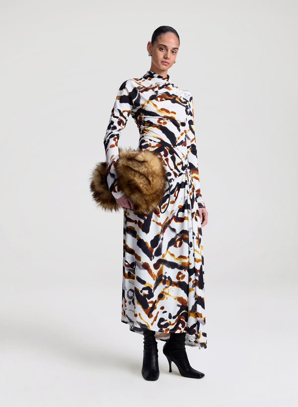 Woman wearing a patterned dress holding a faux fur bag on a white background