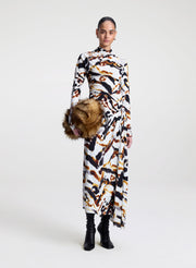 Model wearing a patterned dress with a faux fur bag on a white background