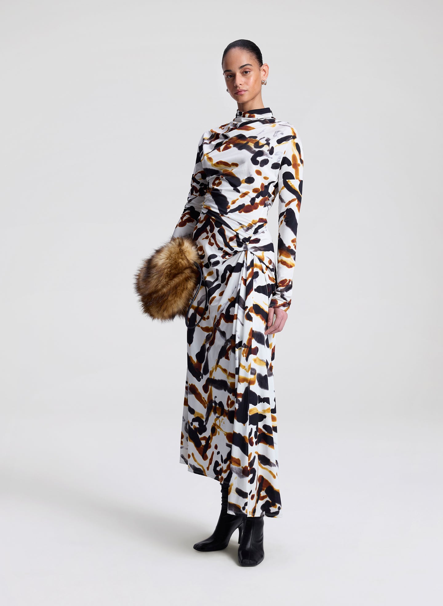 Woman wearing a patterned dress holding a faux fur bag on a white background