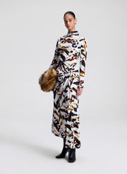Woman wearing a patterned dress holding a faux fur bag on a white background