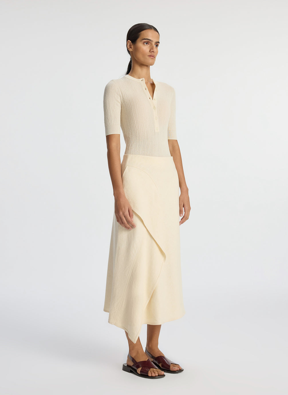 side view of woman wearing beige short sleeve shirt and cream midi skirt