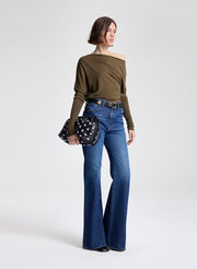 Woman wearing a green off-shoulder top and blue jeans, holding a polka dot bag on a white background