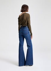 Person wearing blue flared jeans and an olive green top on a white background