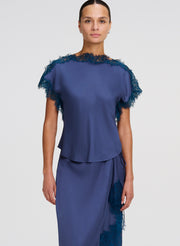 Woman wearing a blue top and skirt with lace details on a white background