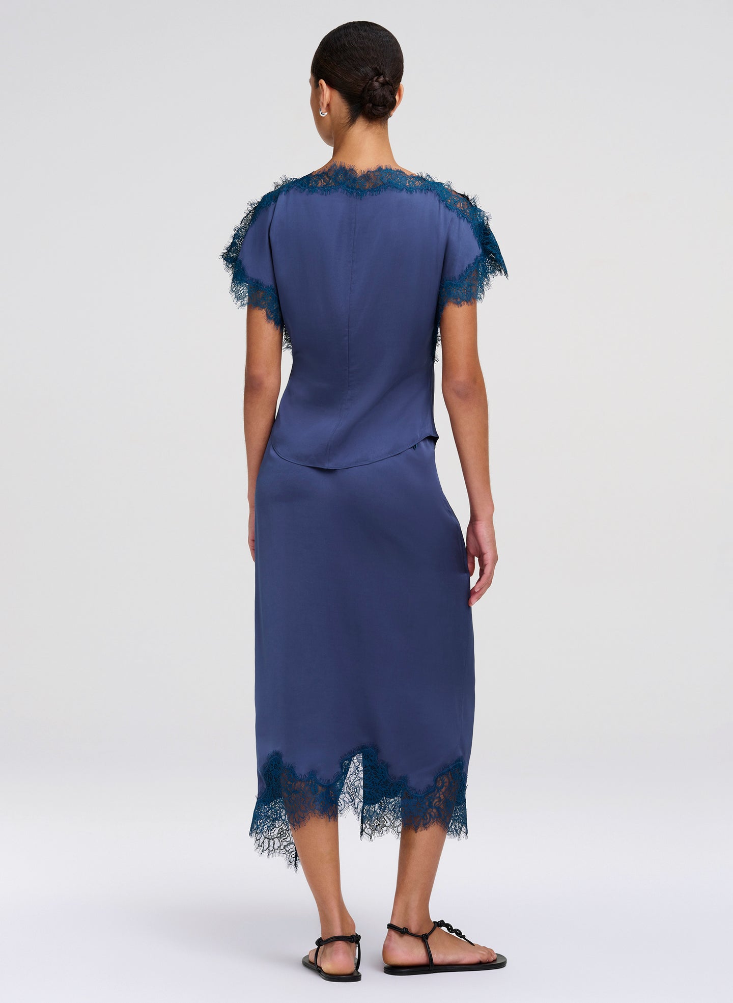 Woman wearing a blue top and skirt with lace details on a white background