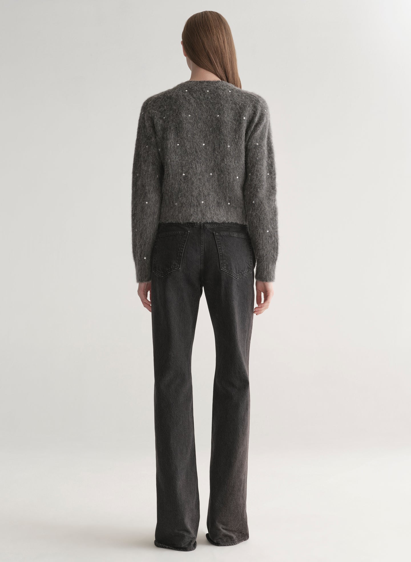 Person wearing a dark gray knit cardigan with embellishments on a plain background