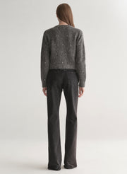 Person wearing a dark gray knit cardigan with embellishments on a plain background