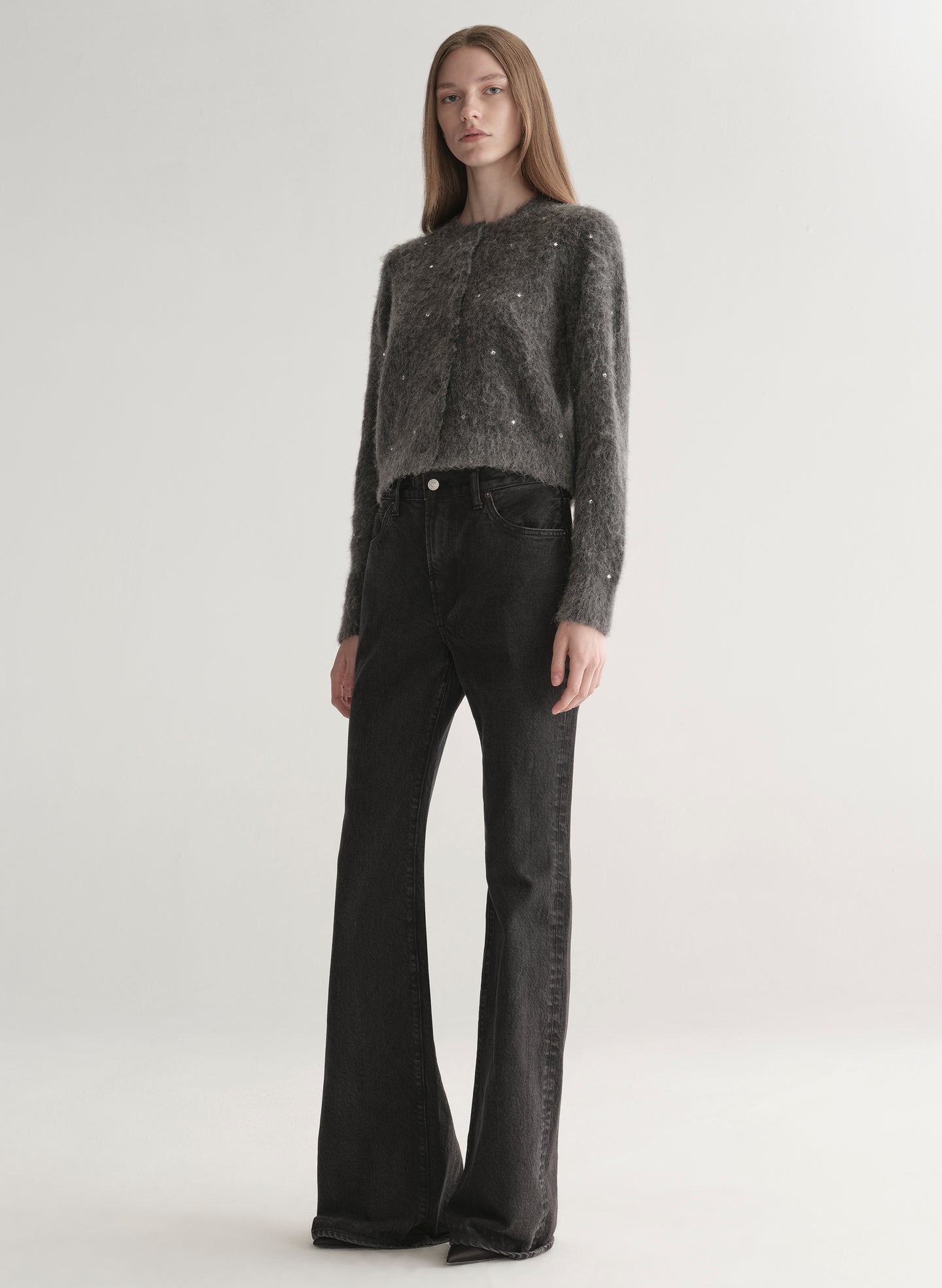 Person wearing a dark gray knit cardigan with embellishments on a plain background