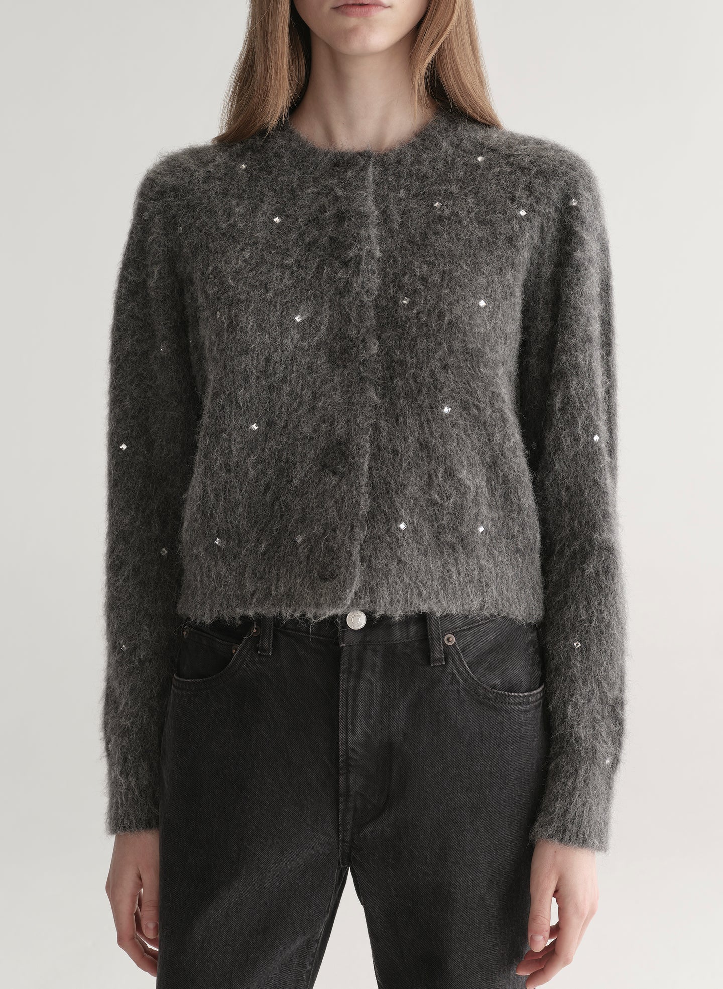 Person wearing a dark gray knit cardigan with embellishments on a plain background