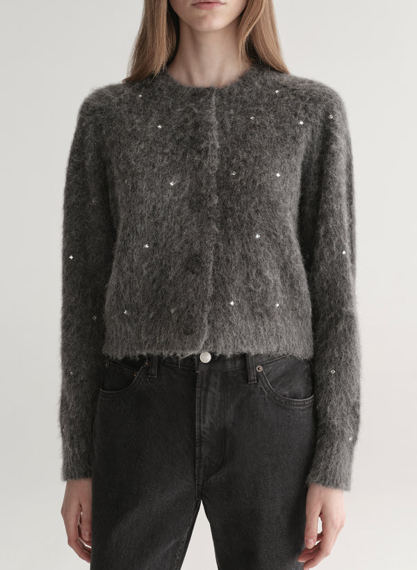 Person wearing a dark gray knit cardigan with embellishments on a plain background