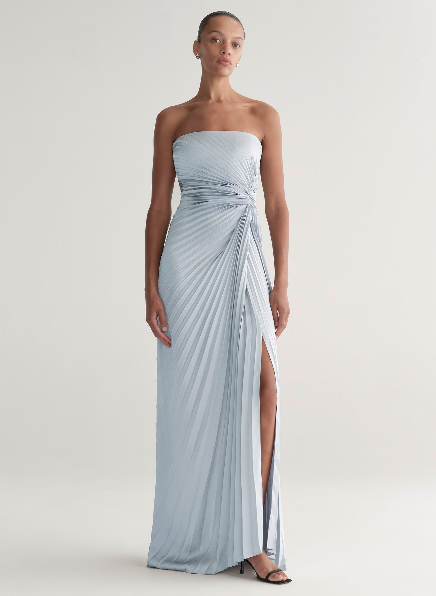 Woman wearing a strapless, light blue gown with a slit on a white background