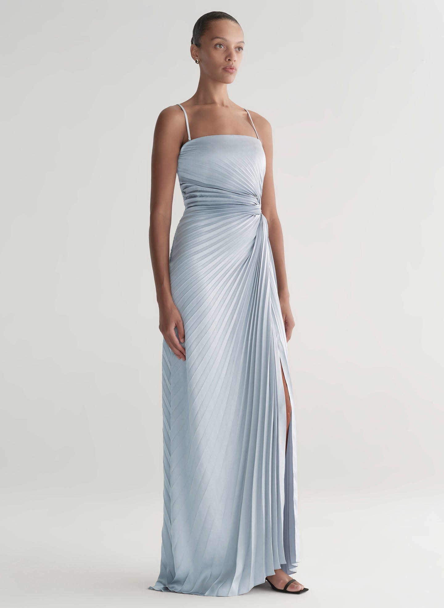 Woman wearing a light blue strapless gown with a slit on a plain background