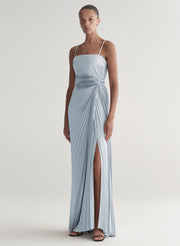 Woman wearing a light blue gown with a slit on a plain background