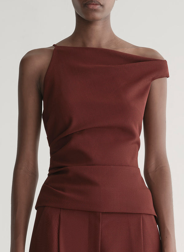 Woman wearing a one-shoulder maroon top and pants against a plain background