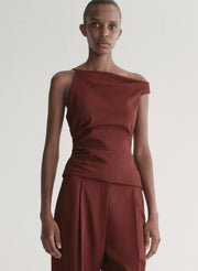 Woman wearing a one-shoulder maroon top and pants against a plain background