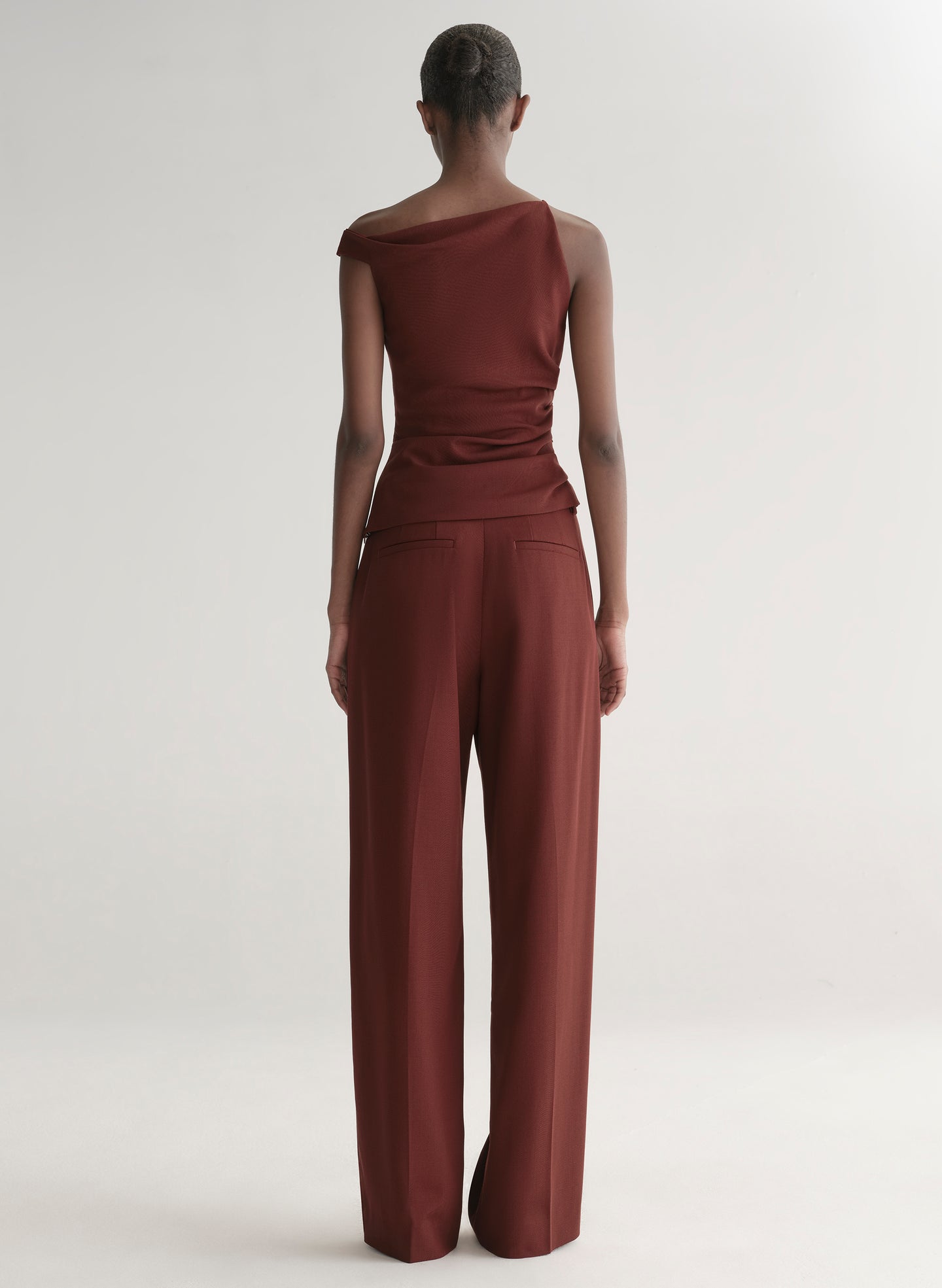 Woman wearing a one-shoulder maroon top and pants against a plain background