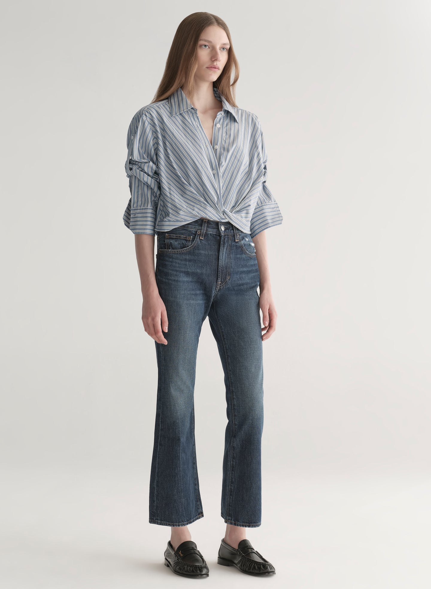 Woman wearing a striped shirt and jeans on a plain background