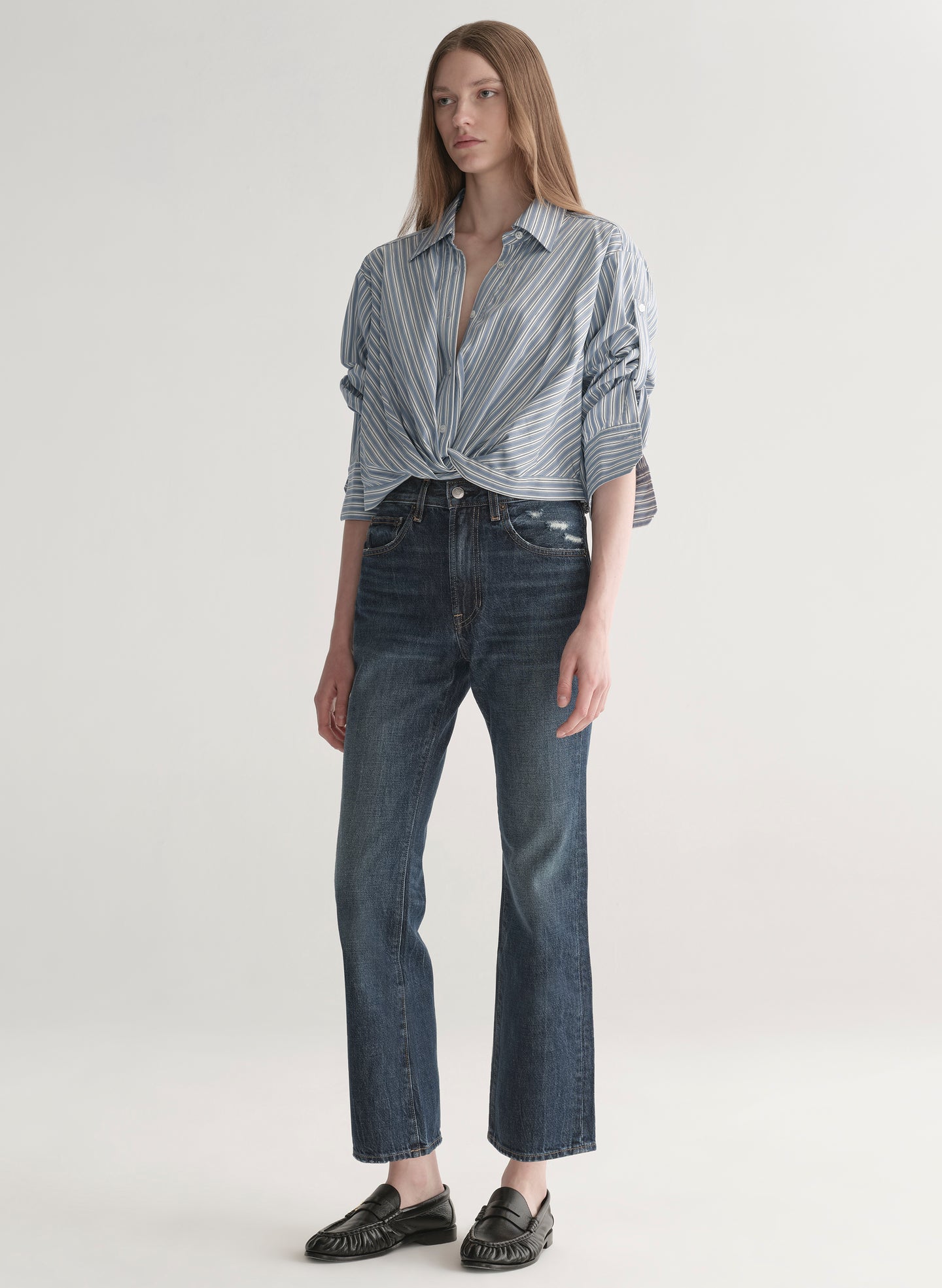Woman wearing a striped shirt and jeans on a plain background