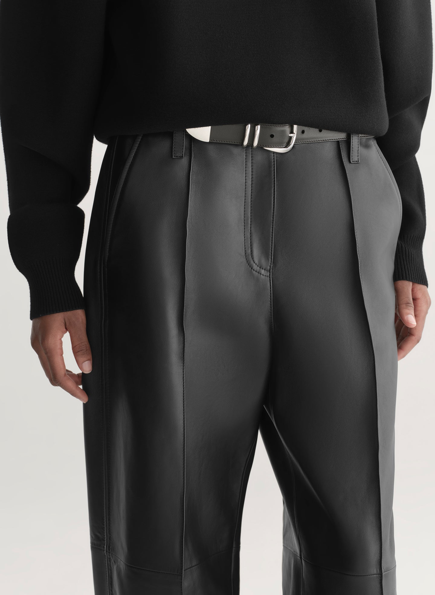 Person wearing a black turtleneck and black leather pants on a light gray background